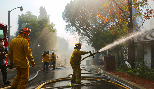 A firefighter sprays water on a burning home in the wealthy Bel-Air neighborhood during the Skirball Fire (Credit: Photo by Mario Tama/Getty Images)
