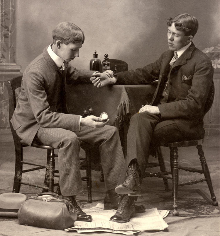 A vintage studio portrait of a young doctor taking a patient's pulse in the late 19th or early 20th century.
