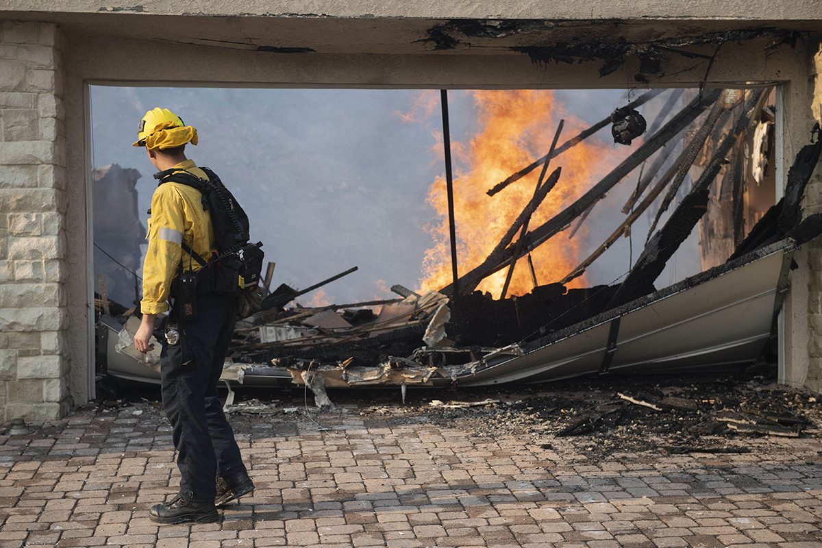 L.A. City Firefighter Zach Duda walks past the burning home of Shane Clark on Hitching Post Lane after the Woolsey fire swept through the Bell Canyon neighborhood of West Hills. (Credit: Getty Images)