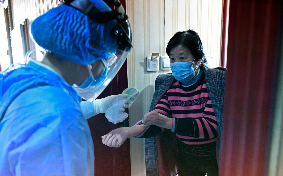 A medical staff member takes temperature for a woman at a hotel arranged as a quarantine center for people returning from overseas countrie (Photo by Wei Liang/China News Service via Getty Images)